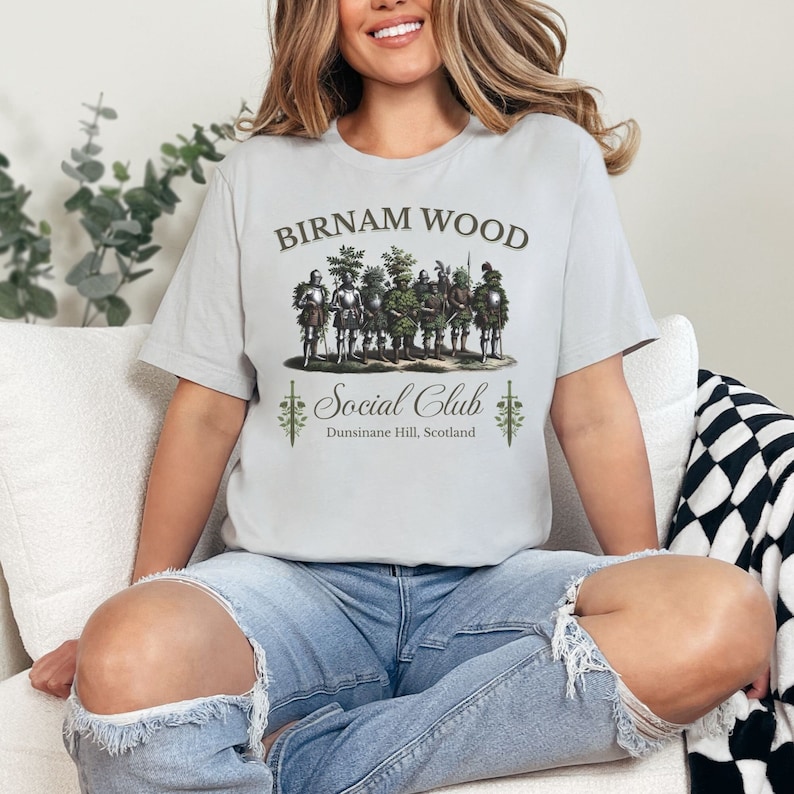 May include: A gray t-shirt with the text "Birnam Wood Social Club" and a graphic of a group of men in armor with trees growing out of their helmets. The text "Dunsinane Hill, Scotland" is below the graphic.