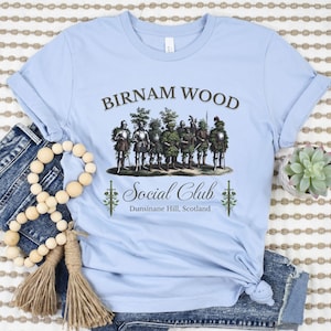 May include: A light blue t-shirt with a graphic of a group of men dressed in armor and foliage, with the text "Birnam Wood Social Club Dunsinane Hill, Scotland".