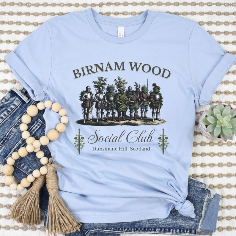 May include: A light blue t-shirt with a graphic of a group of men dressed in armor and foliage, with the text "Birnam Wood Social Club Dunsinane Hill, Scotland".