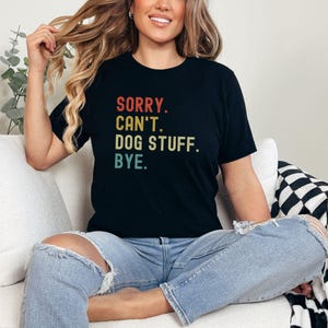 以下が含まれることがあります： 「SORRY. CAN'T. DOG STUFF. BYE.」とヴィンテージスタイルのグラフィックがプリントされた黒いTシャツです