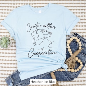 May include: Light blue t-shirt with a black line drawing of a dog's head and the text "Create a culture of Cooperation".