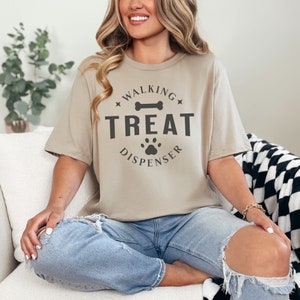 May include: A beige t-shirt with a black graphic that says "Walking Treat Dispenser" with a bone and paw print.