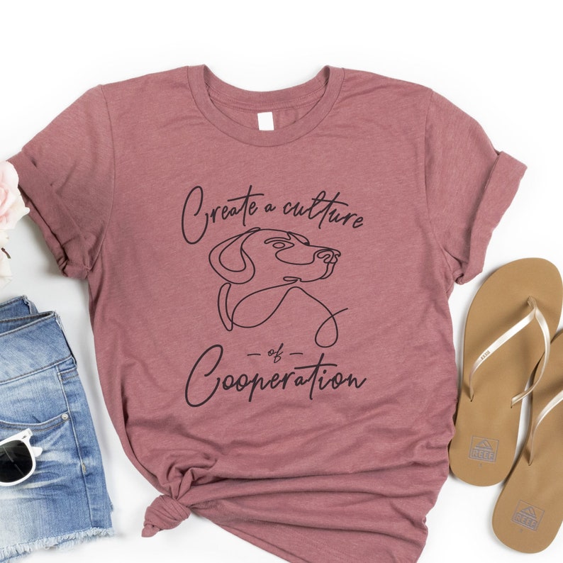 May include: A maroon t-shirt with a black graphic design that says "Create a culture of cooperation" with a line drawing of a dog's head.