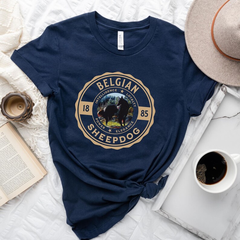 Op de afbeelding: Donkerblauw T-shirt met een beige cirkelvormige afbeelding met een Belgische herder en de tekst "BELGIAN SHEEPDOG" met de woorden "INTELLIGENCE", "LOYALTY", "POWER", "ELEGANCE" en de nummers "18" en "85" rond de cirkel.