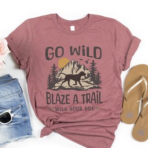 May include: A maroon t-shirt with the text "Go Wild Blaze a Trail with Your Dog" and a graphic of a dog running through a mountain landscape.