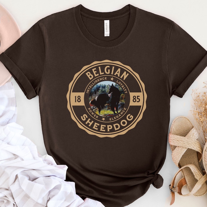 Op de afbeelding: Een bruin t-shirt met een beige cirkelvormige afbeelding met een Belgische herder met de tekst "Belgian Sheepdog" en de woorden "Intelligentie, Loyaliteit, Kracht, Elegantie" rond de hondenafbeelding.