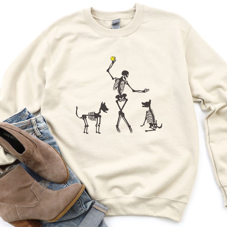 Funny Halloween Dog Sweatshirt. Get ready for the spooky season with this funny Halloween dog lover shirt. With skeleton dog lover, one hand poised to throw a ball, the other directing a skeleton dog to stay. A second spooky dog waits for his turn.