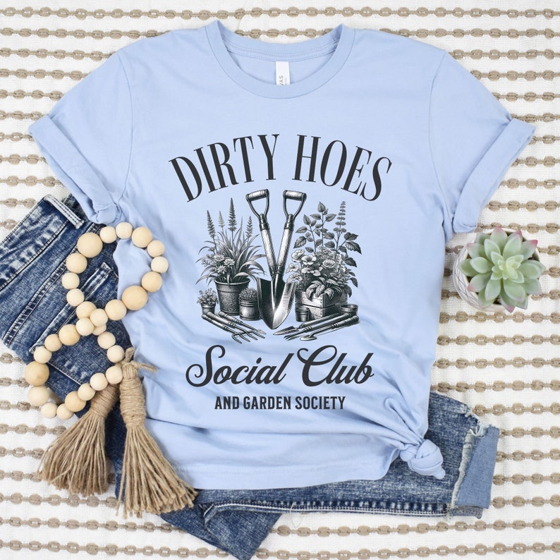 May include: Light blue t-shirt with black text that reads "Dirty Hoes Social Club and Garden Society". The text is surrounded by a black circle and an illustration of gardening tools and plants.