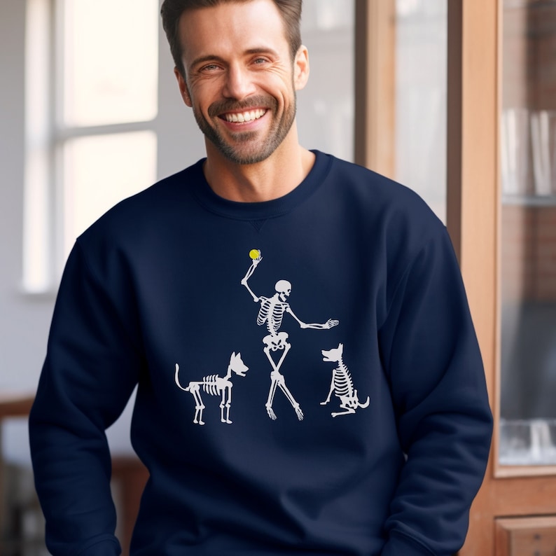 Funny Halloween Dog Sweatshirt. Get ready for the spooky season with this funny Halloween dog lover shirt. With skeleton dog lover, one hand poised to throw a ball, the other directing a skeleton dog to stay. A second spooky dog waits for his turn.