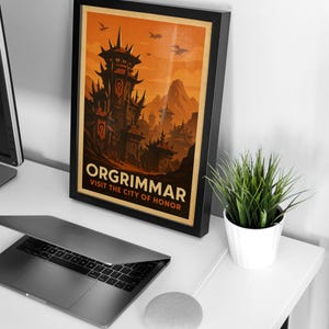 May include: Framed poster featuring the city of Orgrimmar, with a dark, imposing fortress and a fiery orange sky. The text reads "ORGRIMMAR VISIT THE CITY OF HONOR". The poster is in a black frame, displayed on a white desk with a laptop and a small potted plant.
