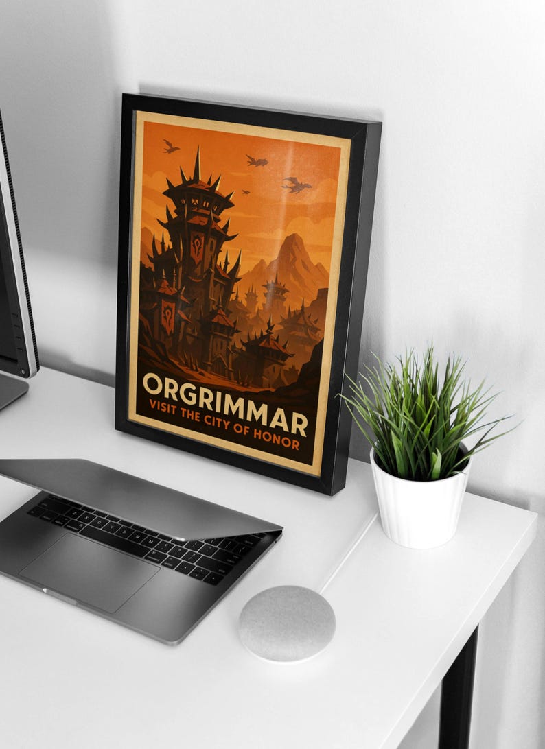 May include: Framed poster featuring the city of Orgrimmar, with a dark, imposing fortress and a fiery orange sky. The text reads "ORGRIMMAR VISIT THE CITY OF HONOR". The poster is in a black frame, displayed on a white desk with a laptop and a small potted plant.