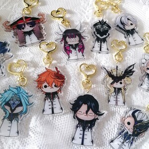 Puede incluir: Una colección de llaveros acrílicos con diseños de personajes de dibujos animados. Cada llavero tiene un cierre dorado en forma de corazón. Los personajes tienen varios colores de pelo y visten abrigos blancos con detalles negros. Los llaveros están sobre una superficie blanca texturizada.
