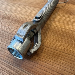 May include: A silver metal tool with a threaded handle and a claw-like grip. The tool has a small ring attached to the handle.