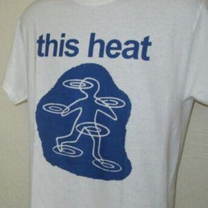 May include: White t-shirt featuring the words "this heat" in blue. Beneath the text is a blue shape with a white outline of a figure with circular designs. The shirt has a crew neck and short sleeves.
