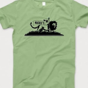 Könnte beinhalten: Ein grünes T-Shirt mit einer schwarzen Grafik eines Löwen, der eine Flagge mit der Aufschrift "Wackie's" hält.