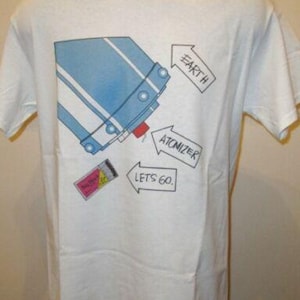 Puede incluir: Camiseta blanca con un diseño gráfico azul y blanco. El diseño incluye flechas que apuntan a las palabras "Earth", "Atomizer" y "Lets Go."