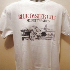 May include: White t-shirt with the red text "BLUE OYSTER CULT SECRET TREATIES". The shirt has a black and white graphic of an aircraft and figures beneath the text.