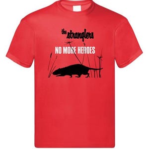 May include: Red t-shirt featuring the text "the stranglers" above "NO MORE HEROES" in white. A black silhouette of a rat is below the text, with tall grass in the background. The shirt is a crew neck.