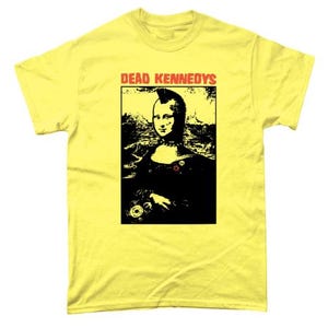 May include: Yellow t-shirt featuring a black and white image of a woman with a mohawk, holding a record. The text "DEAD KENNEDYS" is printed in red above the image.