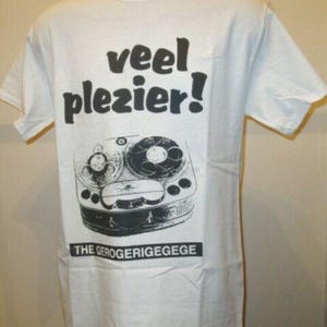 May include: White t-shirt with a black graphic of a vintage reel-to-reel tape recorder. The shirt features the text "veel plezier!" above the graphic and "THE GEROGERIGEGEGE" below it.
