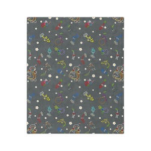 May include: A gray blanket with a repeating pattern of colorful cartoon characters, flowers, and other shapes. The characters are outlined in various colors, including yellow, red, and blue. White flowers are scattered throughout the design.