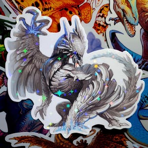 May include: A holographic sticker featuring a detailed illustration of a white and gray mythical creature with wings spread wide. The creature has a fierce expression and appears to be in mid-flight. The sticker has a sparkly, iridescent finish.