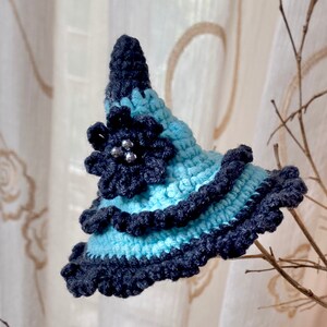 May include: A blue and grey crocheted witch hat with a black flower and silver beads.