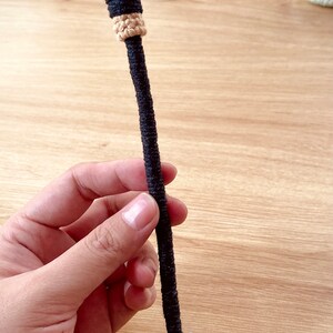 May include: A small, crocheted broom with a brown handle and a blue bow. The broom is made of beige yarn and has a black band around the handle.