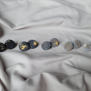 Könnte beinhalten: Ein Set mit sechs runden Ohrsteckern mit Marmorierung und goldenen Flocken. Die Ohrringe sind in drei Farben: Schwarz, Grau und Weiß.
