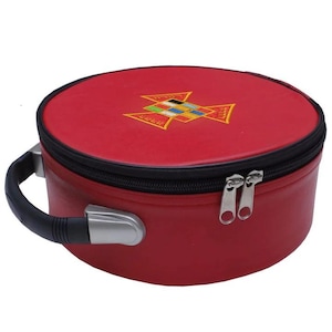 May include: A round, red case with a black zipper and handle. The case features an embroidered emblem on the top and two silver zipper pulls. The handle is black with a silver metal accent.