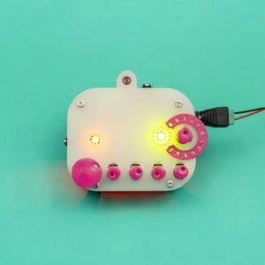 May include: A white rectangular electronic device with rounded corners, featuring five pink knobs, a pink semi-circular dial, and two glowing yellow LED lights. The device is secured with silver screws and connected to a black power cable with red and black wires.