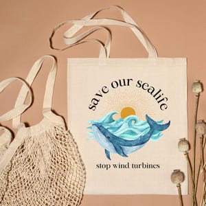 May include: Beige tote bag with a whale illustration and the text "save our sealife" and "stop wind turbines". The whale is blue, with blue waves and a yellow sun in the background. A beige net bag is on the left.