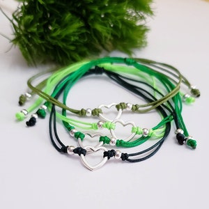 May include: Set of five friendship bracelets with green and black cords and silver heart charms.