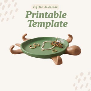 Puede incluir: Una bandeja con forma de tortuga, centro circular verde y extremidades color canela. El texto "digital download Printable Template" aparece arriba. Dentro de la bandeja hay pendientes de aro dorados, un collar de perlas, un anillo y una pinza.