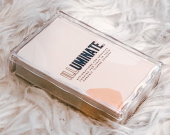 May include: A deck of cards in a clear plastic case. The cards have a light pink background with the word "ILLUMINATE" in a bold, modern font. Text below reads "Affirmations for Spoonies, Looking for Light in their Chronic Illness Journey."