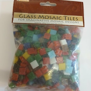 May include: A clear plastic bag containing assorted square glass mosaic tiles in various colors including red, green, blue, yellow, and white. The header card reads Glass Mosaic Tiles for Imaginative Mosaic Designs with contents .45kg/16oz glass tile pieces.