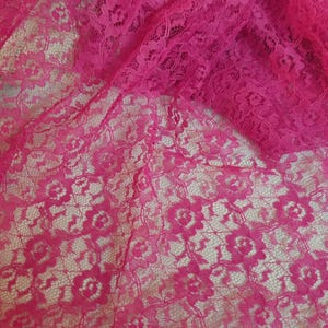 A close-up, overhead shot of fuchsia floral lace fabric, with a section of the fabric gathered at the top right.