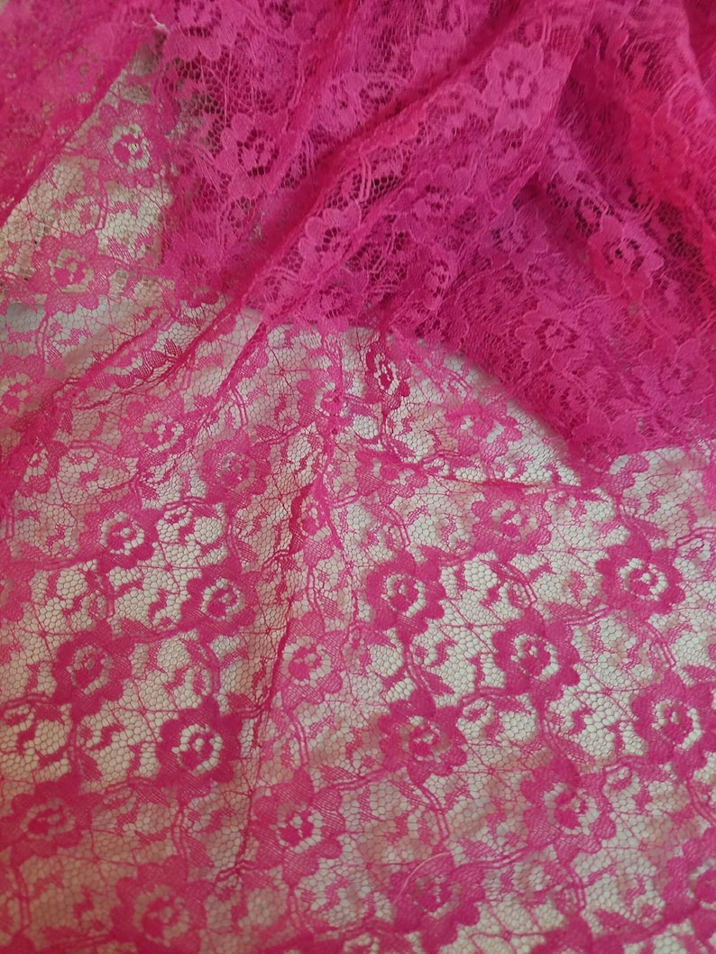A close-up, overhead shot of fuchsia floral lace fabric, with a section of the fabric gathered at the top right.