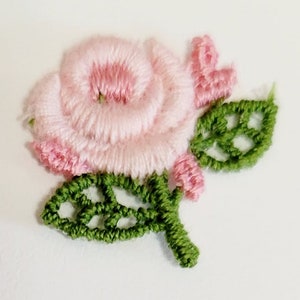 May include: A pink embroidered rose with green leaves. The rose is made of yarn and has a delicate, feminine look.