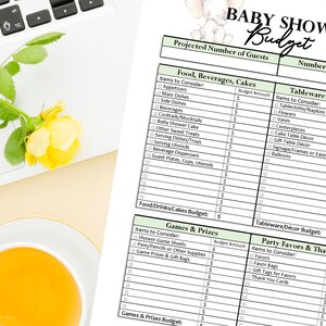 May include: A baby shower budget planner with sections for food, decorations, and games. The document is on a white surface with a laptop, a yellow rose, and a cup of orange liquid. The title "BABY SHOWER Budget" is at the top.