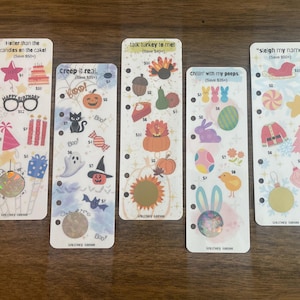 May include: Five decorative scratch-off cards with holiday themes. The cards feature illustrations of birthday, Halloween, Thanksgiving, Easter, and Christmas symbols. Each card has a unique phrase at the top and a scratch-off circle at the bottom.
