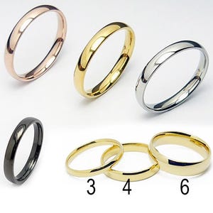 Könnte beinhalten: Eine Sammlung von sechs Ringen in verschiedenen Metallausführungen: Roségold, Gold, Silber und Schwarz. Die Ringe sind schlichte Bänder mit glatter, polierter Oberfläche. Die Ringe werden vor weißem Hintergrund präsentiert.