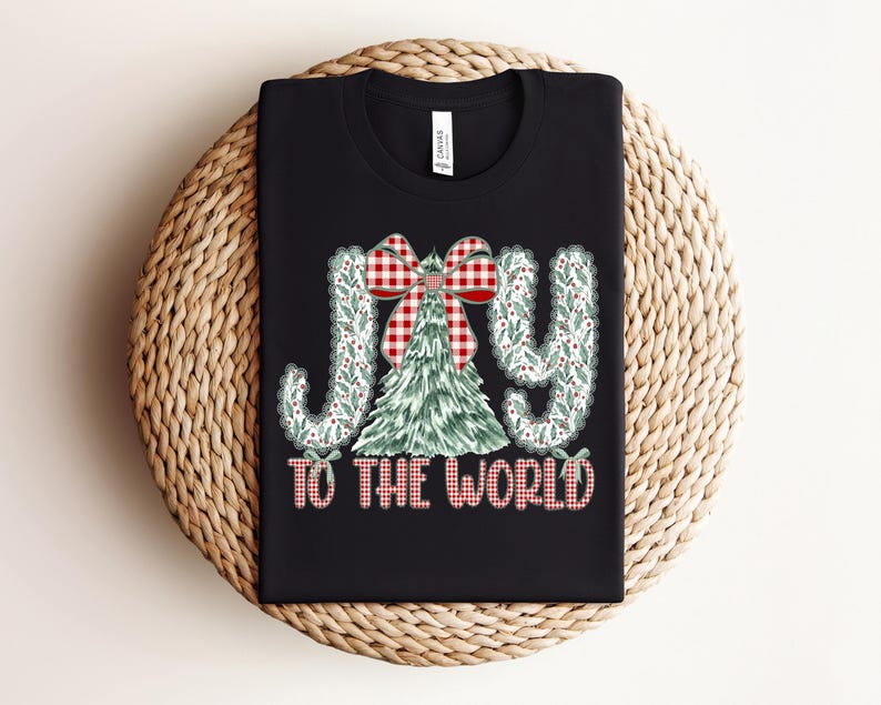 May include: Black t-shirt with the words "JOY TO THE WORLD" in a festive design. The word "JOY" is in a decorative font with a green and white pattern. A Christmas tree and a red and white plaid bow are in the center.