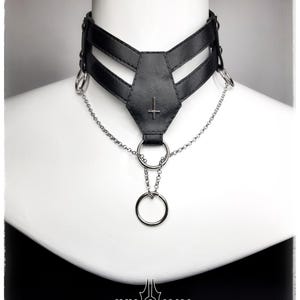 May include: Black choker necklace with a silver chain and rings. The choker features a geometric design with a cross symbol. The brand name "ANN NOX" is displayed at the bottom.