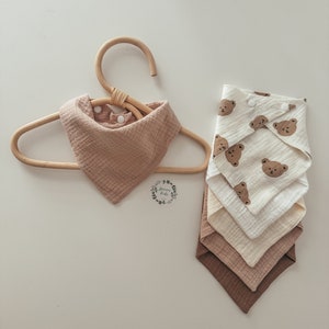 May include: Set of five brown and white muslin baby bibs with a bear print. The bibs are folded and stacked on top of each other. The top bib has a white background with brown bear faces printed on it. The other bibs are solid brown and white.