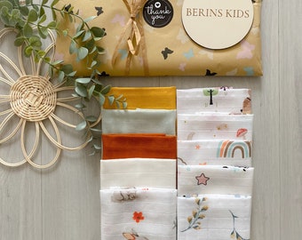 May include: A set of eight white muslin baby burp cloths with different patterns. The patterns include a rainbow, stars, a bunny, and leaves. The cloths are packaged in a brown paper gift bag with a "Thank You" sticker and a wooden circle with the text "Berins Kids".