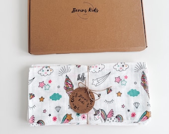 May include: A set of white muslin baby burp cloths with a colorful unicorn, ice cream cone, and star pattern. The cloths are folded and tied with twine and a brown tag that reads "Bering Kids".