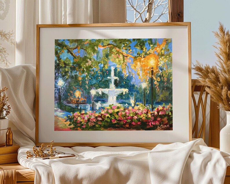 May include: A framed painting of a park scene with a white fountain, lush greenery, and colorful flowers. The artwork features a warm color palette with a focus on light and shadow, creating a serene atmosphere. The artist's signature is visible in the lower right corner.