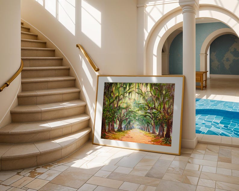 May include: A framed landscape painting of a tree-lined path with sunlight filtering through the branches. The artwork has a gold frame and is leaning against a wall in a bright interior with a staircase and arched doorways.