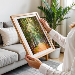 May include: A framed landscape painting showing a path through a forest, with trees lining the sides and sunlight filtering through the leaves. The artwork has a wooden frame and a vibrant colour palette of greens, browns, and oranges.